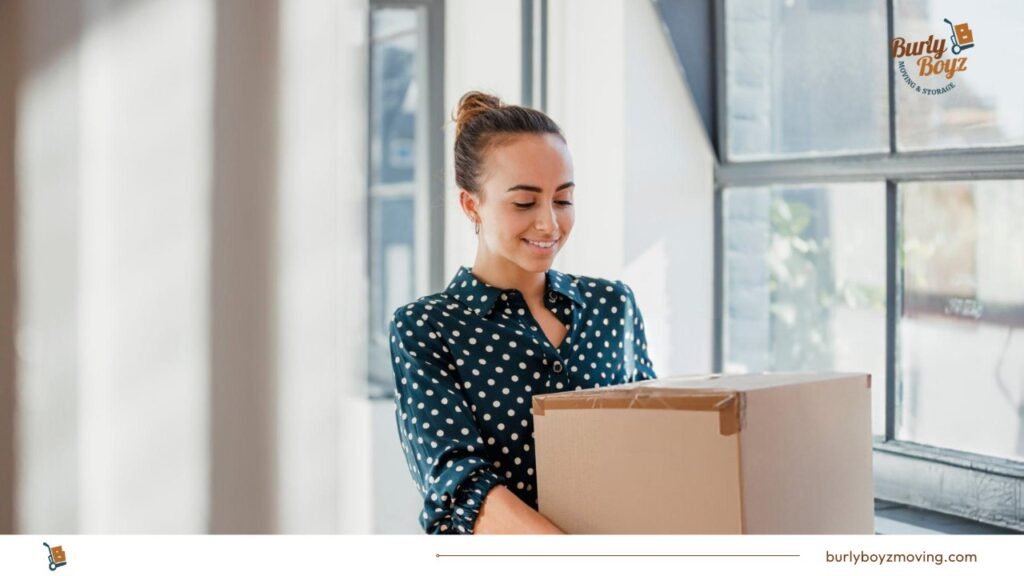 Woman holding a box near window, preparing glass furniture for packing—best ways to pack glass furniture.