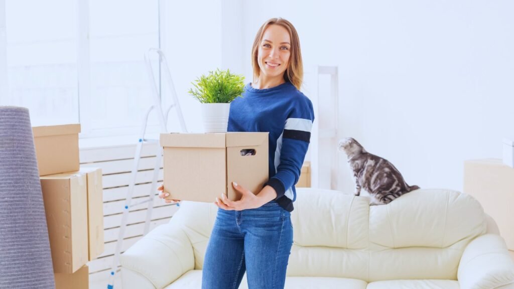 Woman holding moving box with cat on couch  – preparing for moving across the country with cats